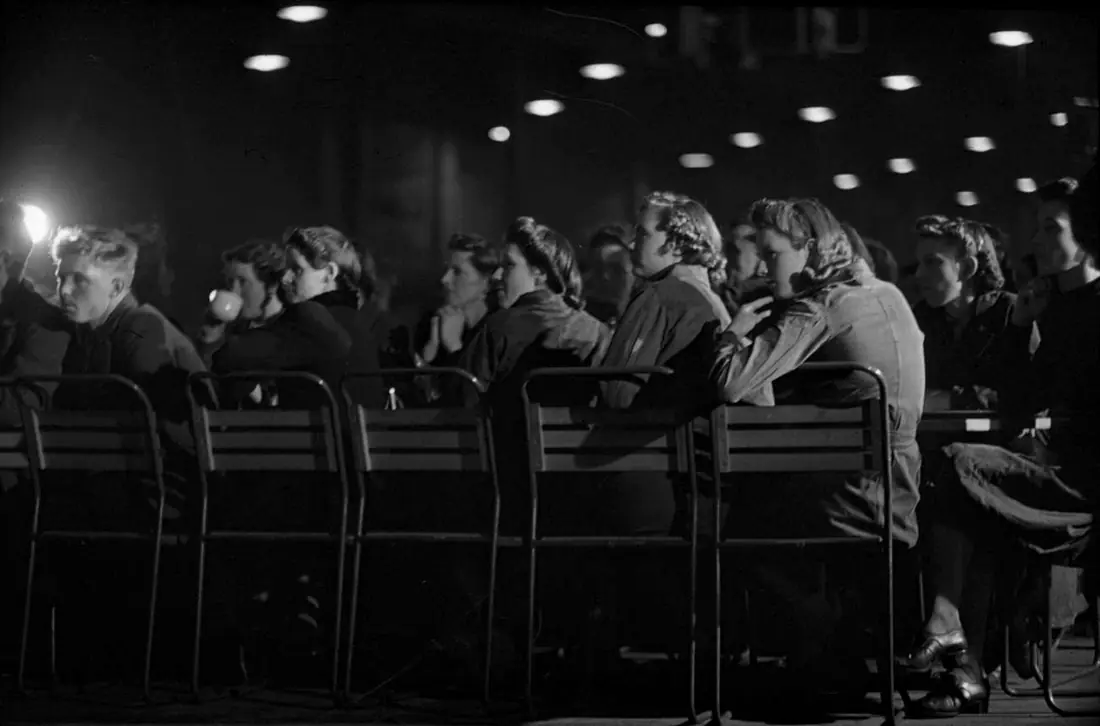 Rows of war workers, seated and watching a lunchtime entertainment in a canteen
